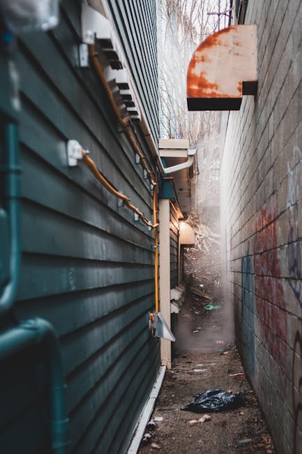 A large, weathered beige cloth refuse bag filled with waste materials, leaning against a wall on a narrow, uneven street. The bag appears overloaded, with a pair of shoes or footwear resting on top, p